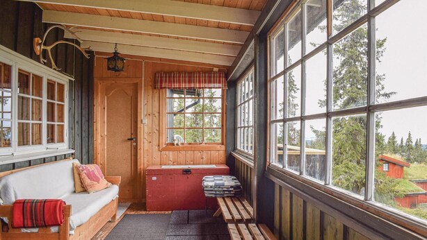 Un accogliente interno di una baita con una panca di legno, una panca imbottita, un baule rosso e una finestra con vista sull'esterno.