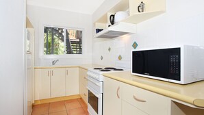 Une cuisine compacte avec des meubles blancs, une cuisinière, un four, un four à micro-ondes et une fenêtre donnant sur une terrasse en bois.