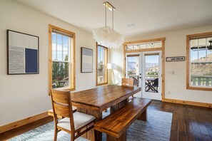 A dining area with a wooden table and benches, framed artwork, and a view of the outdoors.
