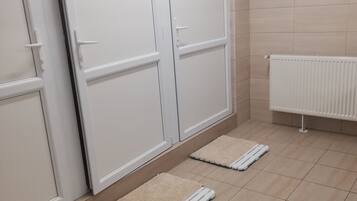 A bathroom with white tiled walls, a white radiator, and two white mats on the floor.