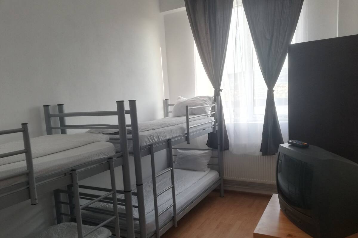 Une chambre avec des lits superposés, un téléviseur posé sur une table en bois et une fenêtre avec des rideaux.