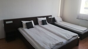 Une chambre d’hôtel avec deux lits simples, une tête de lit en bois, une fenêtre avec des rideaux légers et un plancher en bois.