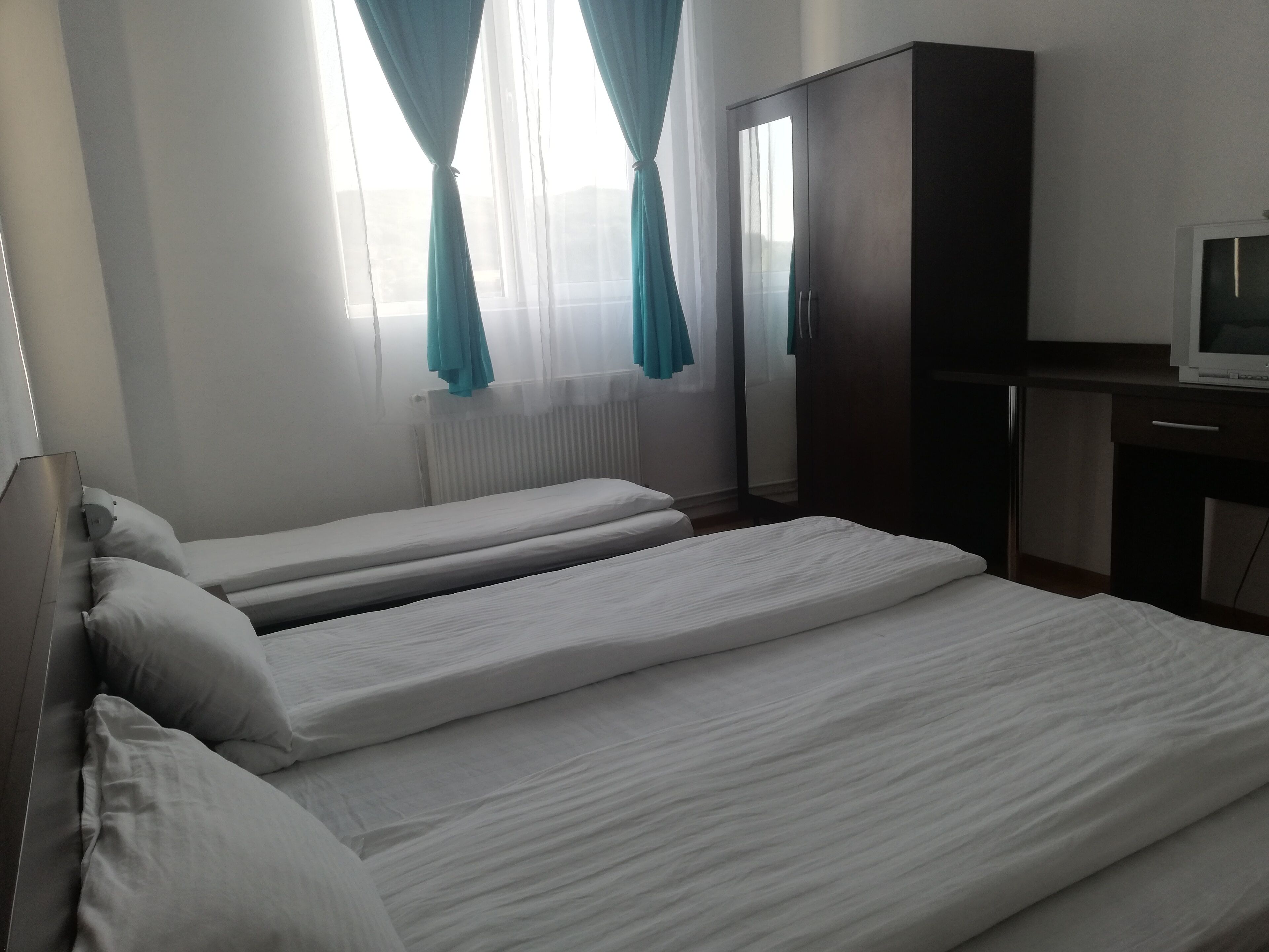A hotel room with two single beds, a wardrobe, a desk with a television, and a window with curtains.