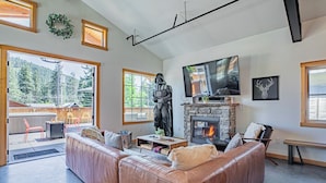 A modern living room with a leather sofa, a stone fireplace, a television, and a statue.