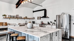 A modern kitchen with a large island, stainless steel appliances, and a wooden bar stool seating area.