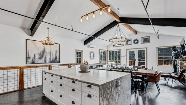 A spacious kitchen with a marble island, wooden beams, and pendant lighting.