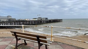 A bench by the seaside with a pier in the background.
