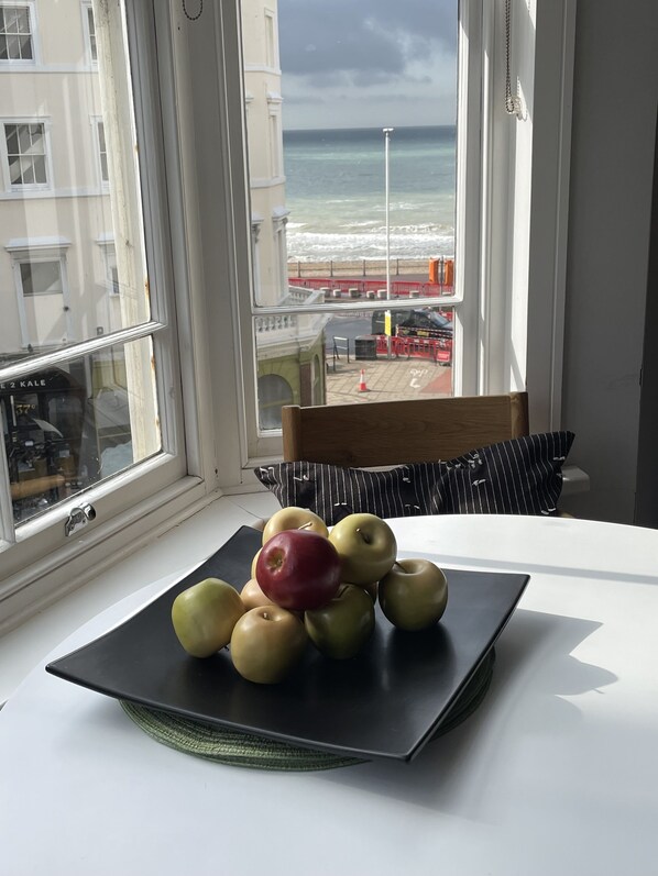 A table with a fruit bowl containing apples, a chair, and a view of the beach and ocean through a window. - * Stylish * Central * Sea View * Modern (Hastings)