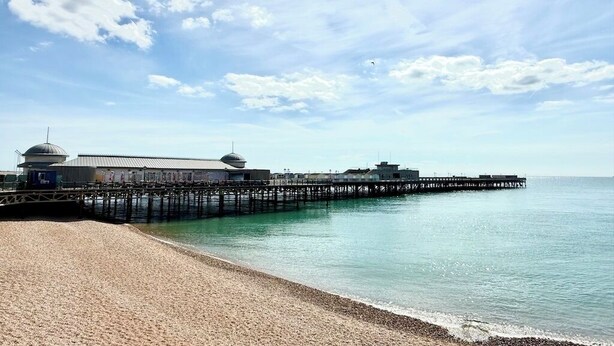 A beach with a pier extending into calm waters, a building with a dome structure, and a clear sky.