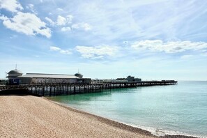 A beach with a pier extending into calm waters, a building with a dome structure, and a clear sky. - * Stylish * Central * Sea View * Modern (Hastings)