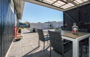En udendørs terrasse med et bord, stole, en flaske og et lille bord med en plante.