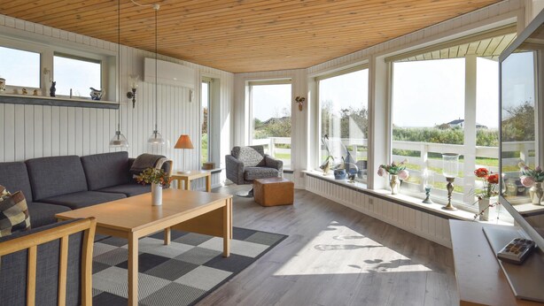 A spacious living room with a wooden ceiling, large windows, a sofa, a coffee table, and a view of the outdoors.