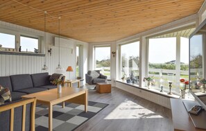 Ein geräumiges Wohnzimmer mit Holzboden, großen Fenstern, einem Sofa, einem Couchtisch und Blick ins Freie.