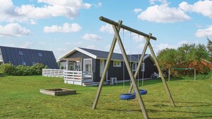 A wooden swing set with tire swings in a grassy yard with a house in the background.