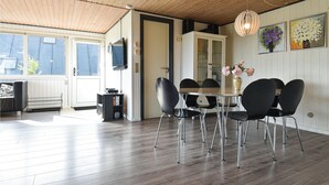 A dining area with a wooden ceiling, a round table with chairs, a TV mounted on the wall, and a window with blinds.