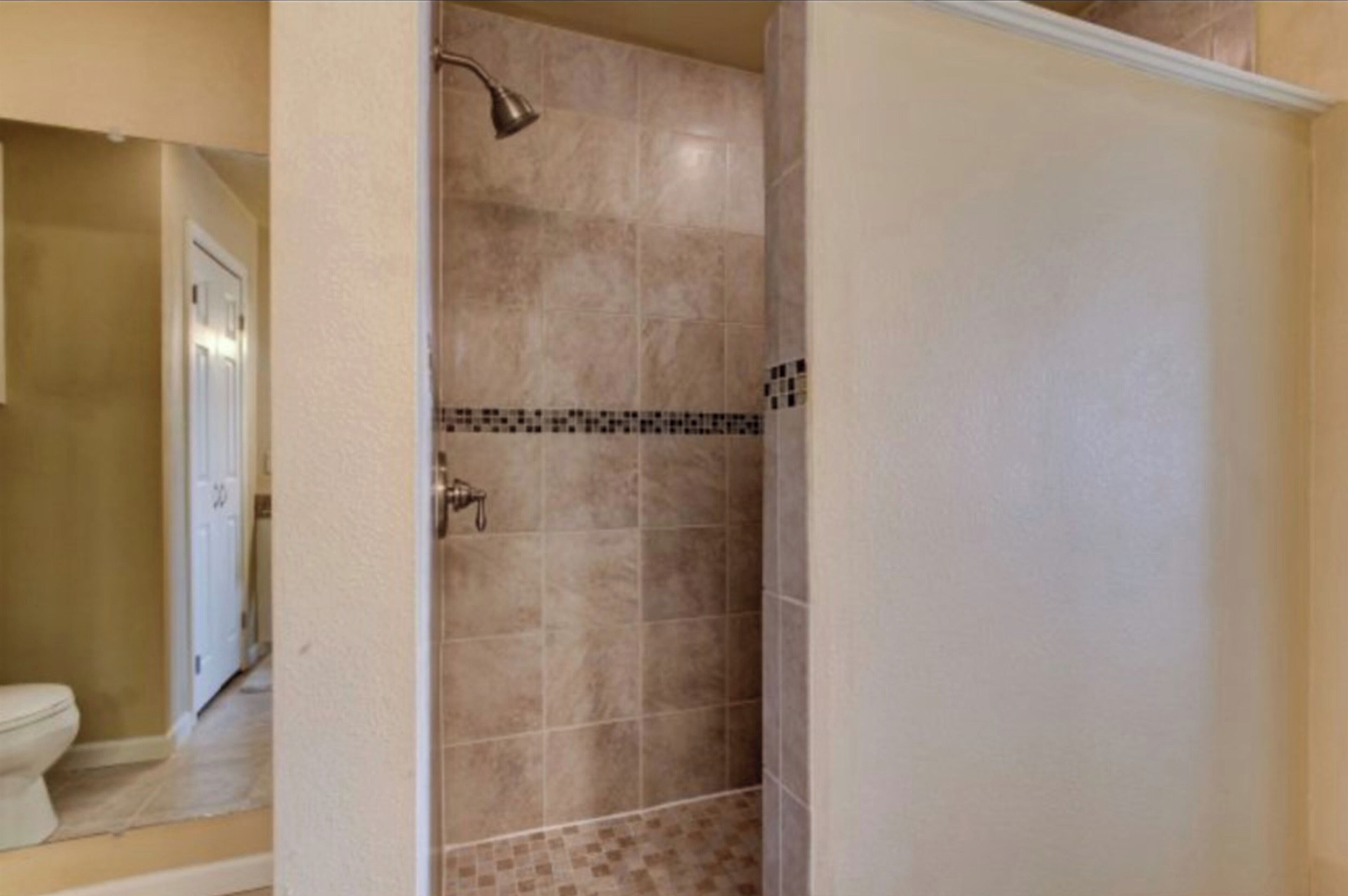 A bathroom with a shower, a toilet, and a tiled floor.
