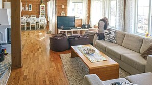 Una sala de estar acogedora con un sofá, una mesa de centro y un televisor. En el fondo, se aprecia un comedor con una mesa y sillas.