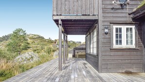 Una terraza de madera que conduce a una cabaña con un porche cubierto, una ventana de marco blanco y un farol en la pared.