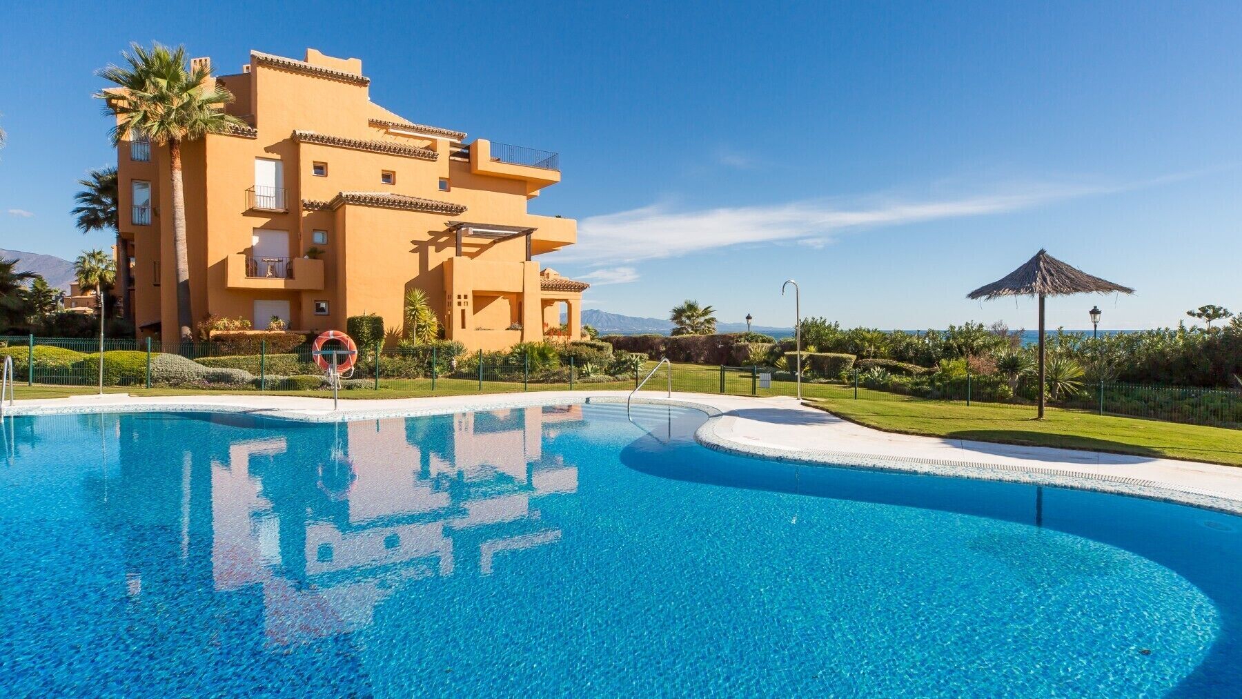 A hotel with a swimming pool, palm trees, and a clear blue sky.