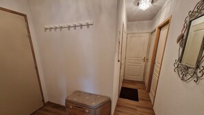 A hallway with wooden flooring, a small chest, a coat rack, a door, and a mirror on the wall. - Spacious 4-room apartment for 6 - 3 bedrooms - 65m2 - Balcony - Near cable car (Valfréjus)
