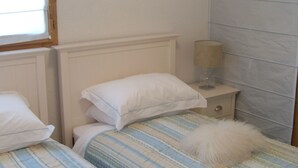 A bedroom with two beds, each with striped bedding and white pillows. There is a bedside table with a lamp and a small drawer. - Spacious 4-room apartment for 6 - 3 bedrooms - 65m2 - Balcony - Near cable car (Valfréjus)
