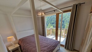 A bedroom with a four-poster bed, a bedside table with a lamp, and a view of a balcony with curtains. - Spacious 4-room apartment for 6 - 3 bedrooms - 65m2 - Balcony - Near cable car (Valfréjus)
