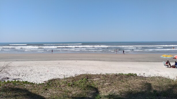 Ein Strand mit blauem Himmel, Wellen und einigen Personen.