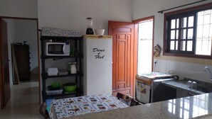 Eine Küche mit Mikrowelle, Kühlschrank und Spüle. Eine Tür trägt ein Schild mit der Aufschrift 'Deus e Fiel'.