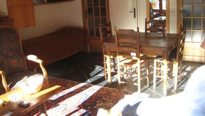 A cozy living room with a wooden dining table, chairs, a sofa, and a television on a shelf.