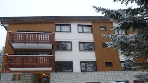 A multi-story building with a brick base and wooden upper floors, featuring balconies and windows.