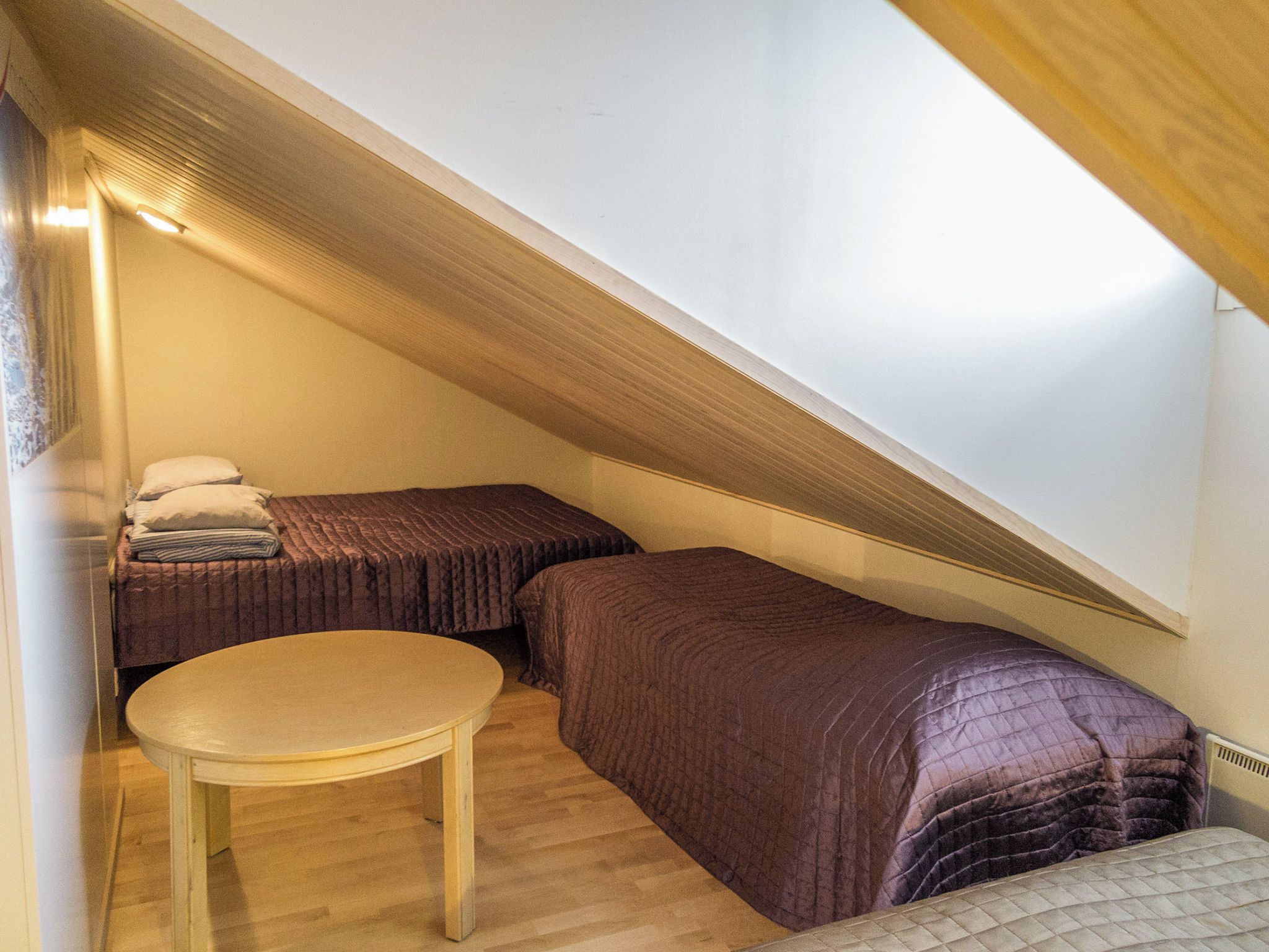 Une petite chambre mansardée, chaleureuse et accueillante, avec deux lits, une table ronde et un plafond en pente.