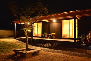 Ein modernes Haus mit einer überdachten Veranda, einem kleinen Garten und einer Bank.