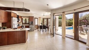 A spacious kitchen with a central island, a dining area with a table and chairs, and a view of a swimming pool through large sliding glass doors. - Villa Tsikkos Dio: Beachfront, Pool, A/C, WiFi (Argaka)