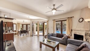 A spacious living area with a sofa, coffee table, and a fireplace. There is a dining area with a table and chairs, and a kitchen with a counter and cabinets. - Villa Tsikkos Dio: Beachfront, Pool, A/C, WiFi (Argaka)