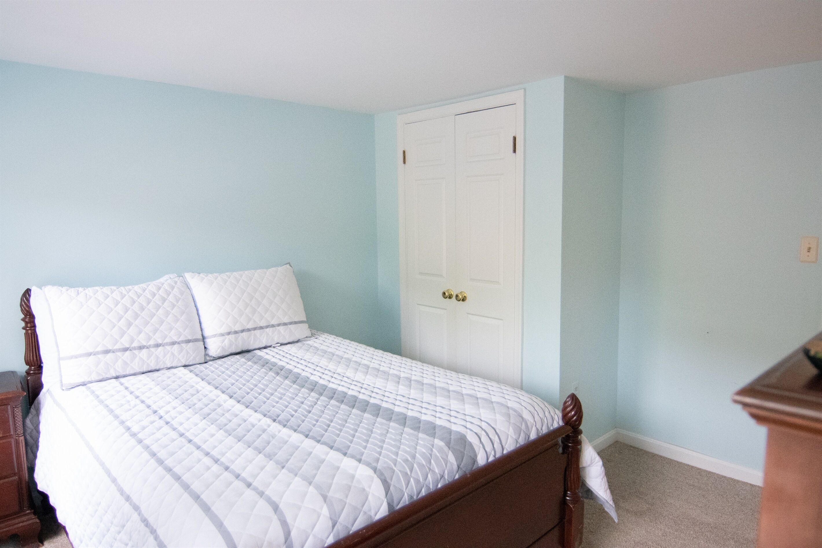 Een slaapkamer met een bed, een houten nachtkastje en een witte deur.