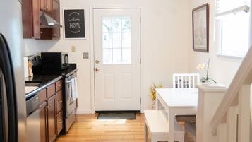 A kitchen with wooden flooring, a white door, and a dining area with a white table and bench.