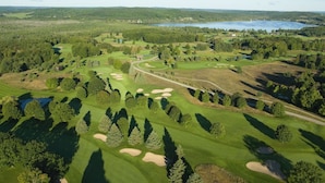 Vista aérea de un campo de golf con varios bunkers, una masa de agua y zonas boscosas circundantes.