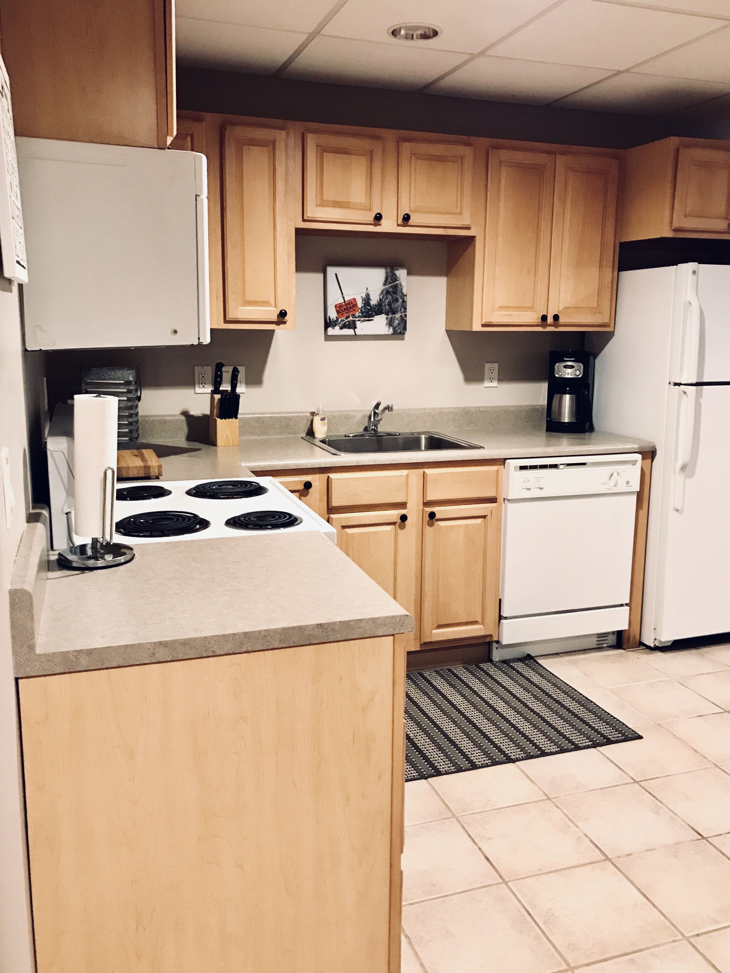 Una cocina con armarios de madera, estufa, fregadero, cafetera y lavavajillas.
