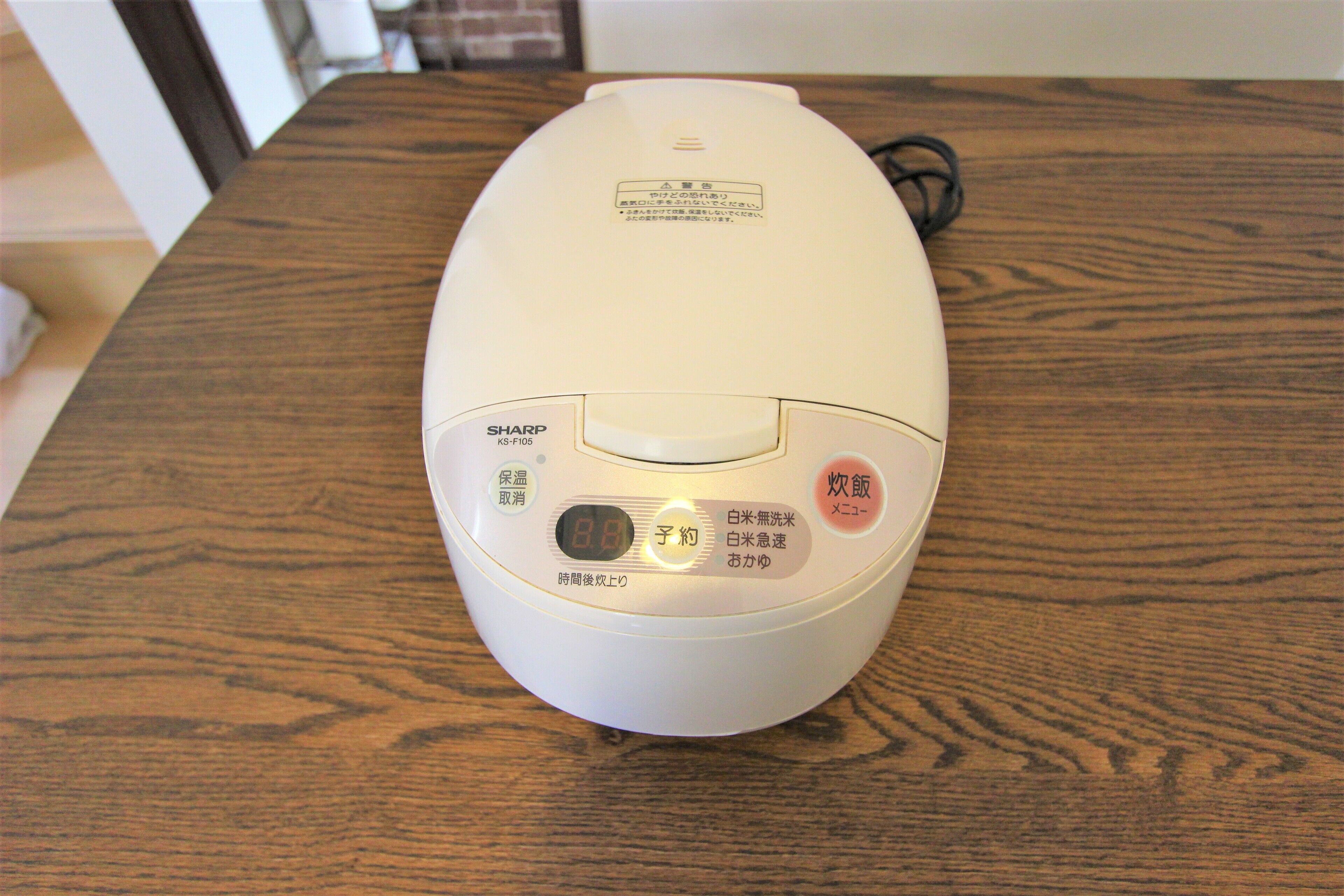 A white rice cooker with a digital display and buttons on a wooden table.
