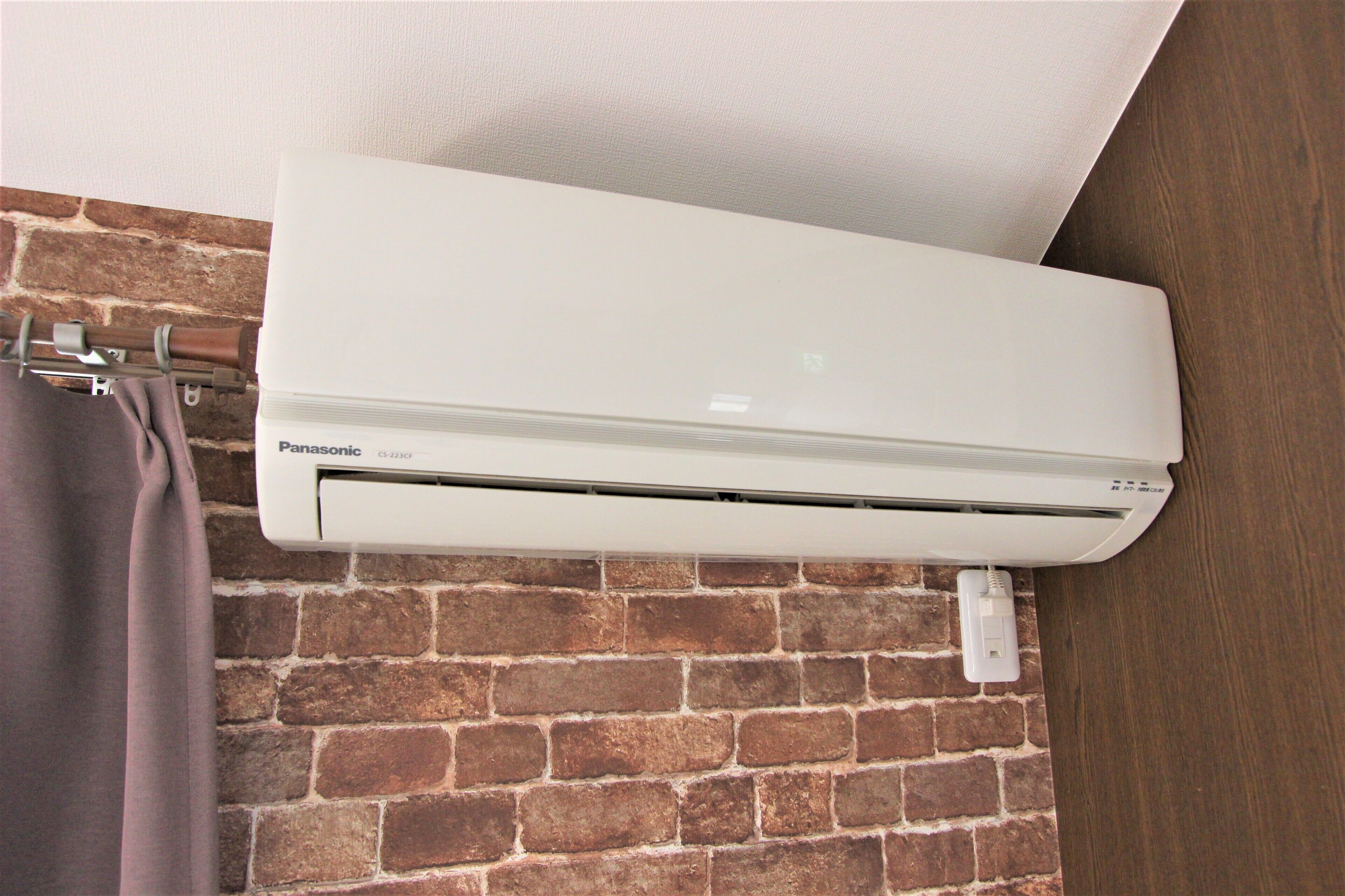 A Panasonic air conditioner mounted on a brick wall.