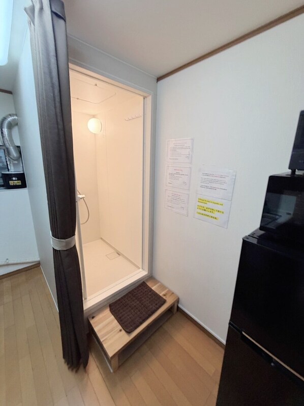 A room with a shower, a small wooden bench, a black cabinet, and a wall with informational notices. - Hotel El Shinjuku 2 (Tokyo)
