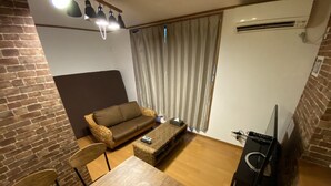 A compact living space with a brown sofa, a wooden dining table, a small coffee table, and a TV stand. - Hotel El Shinjuku 2 (Tokyo)
