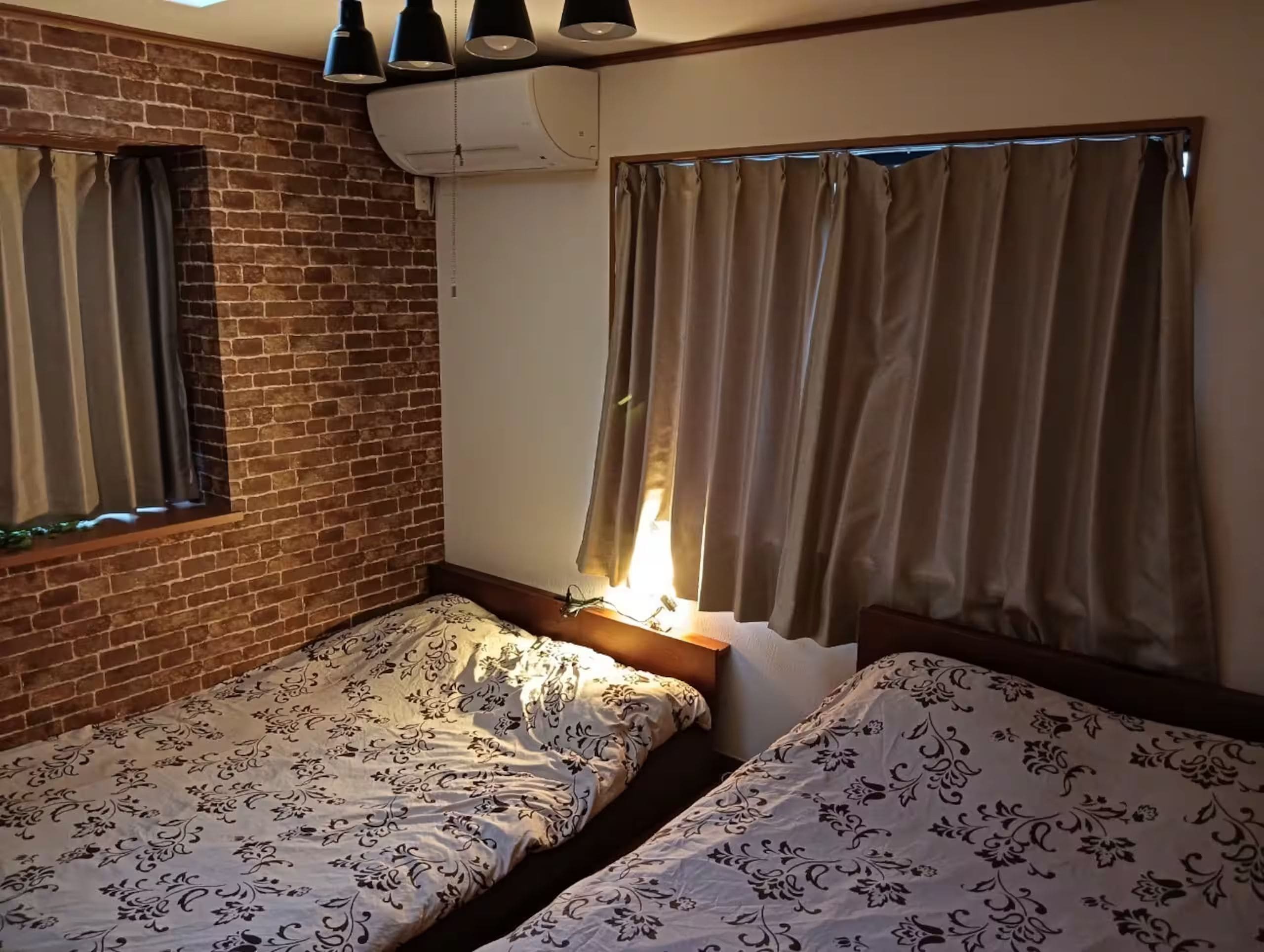 Une chambre avec deux lits, un mur en briques, un appareil de climatisation et des rideaux.