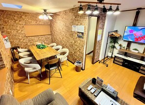 A room with a brick wall, a wooden dining table with chairs, a sofa, a TV, and a floor lamp. - Hotel El Shinjuku 2 (Tokyo)