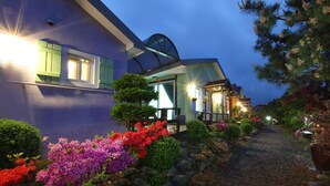 A modern house with a well-maintained garden, a gravel pathway, and a large window with shutters. - Ciel Pension (Yangyang)