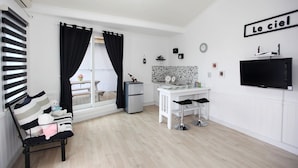 A modern kitchen with a white countertop, a built-in oven, and a microwave. There is a dining area with a white table and two bar stools. A black TV is mounted on the wall, and a black curtain covers the window. - Ciel Pension (Yangyang)