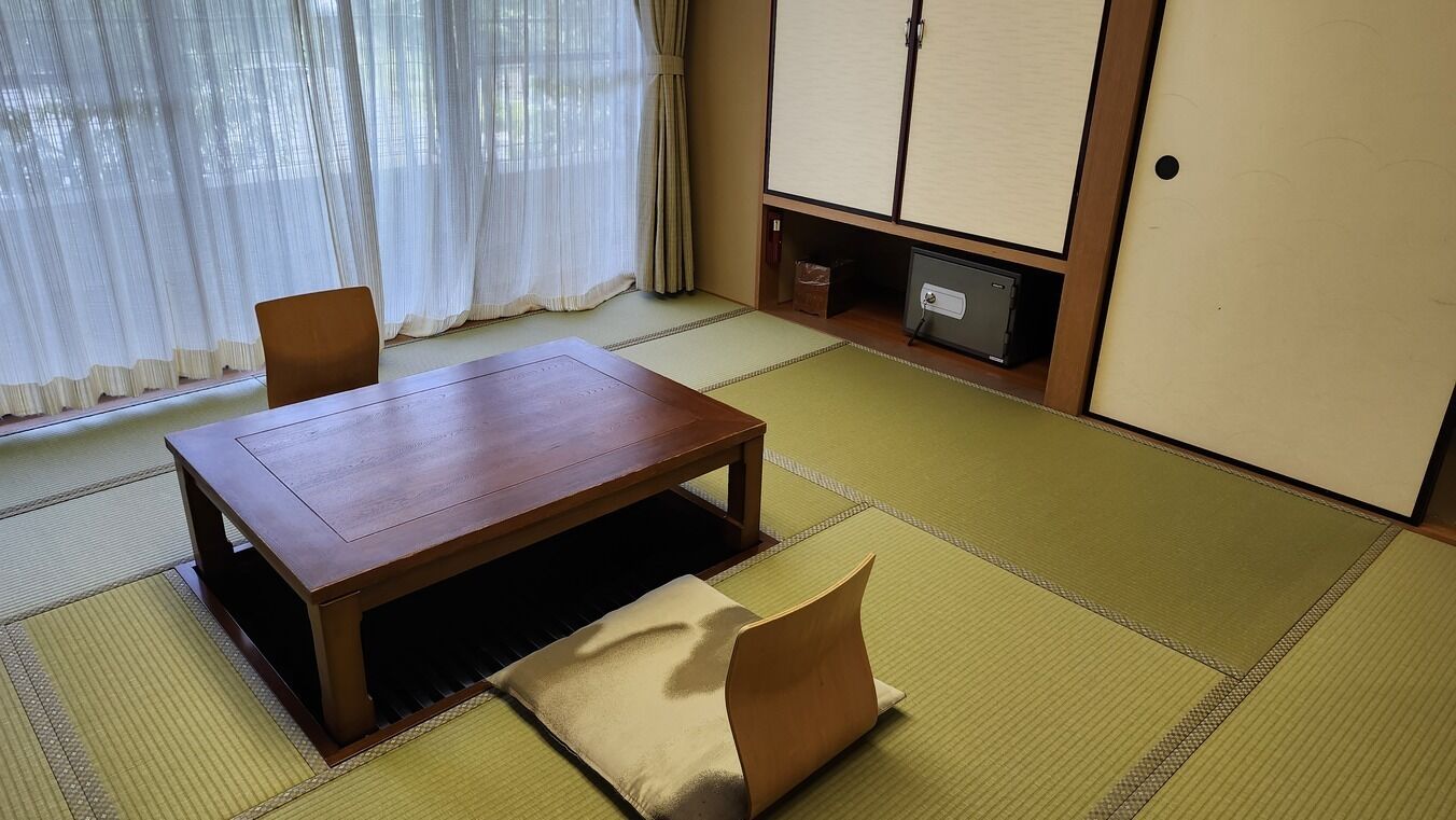 Ein traditioneller japanischer Raum mit Tatami-Böden, einem niedrigen Holztisch, einer gepolsterten Sitzbank und Schiebetüren.
