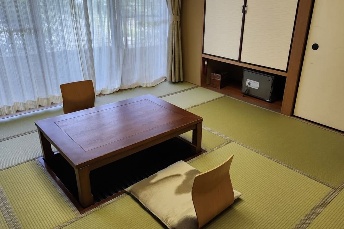 Una habitación japonesa tradicional con suelo de tatami, una mesa de madera baja, un banco acolchado y puertas correderas.