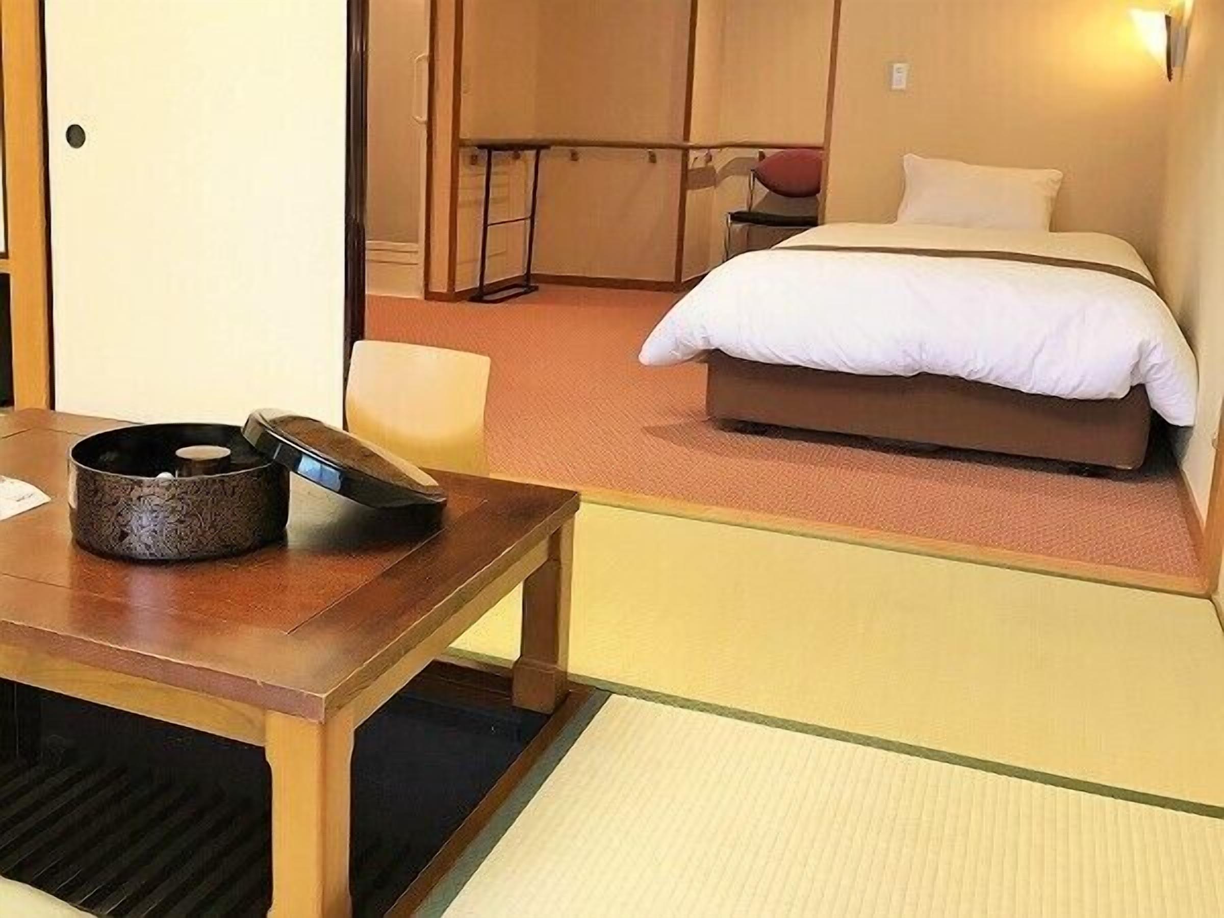 Ein Hotelzimmer mit einem Bett, einem Holztisch mit einer dekorativen Schale, einem Sessel und einem kleinen Tisch mit einem roten Gegenstand.