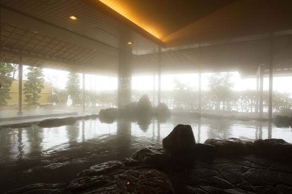 A serene indoor hot spring area with stone rocks and a wooden ceiling. - Kamedake Onsen Tamaminesansou (Okuizumo)